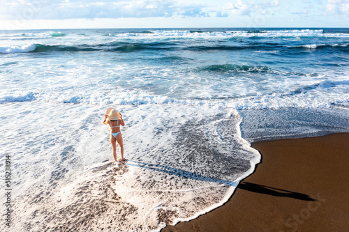 Aerial view of a woman in a bikini at the beach, holding her sun heat, Sao Miguel, Azores, Portugal.