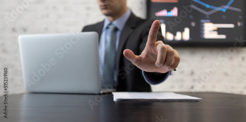 Close-up photo of male hand pointing index finger. Businessman in black suit sitting at the desk and working on laptop in modern office