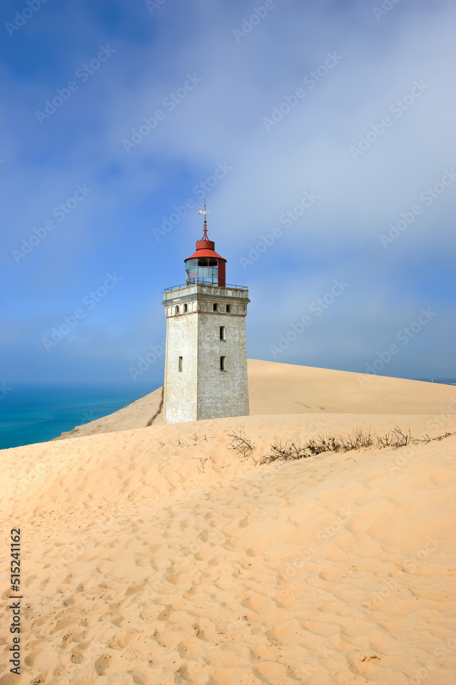 Deserted lighthouse by the sea with blue sky in the background on a sunny day. A lighthouse in between the sandy area surrounded by water and cloudy sky. The mysterious old tower alone in the desert
