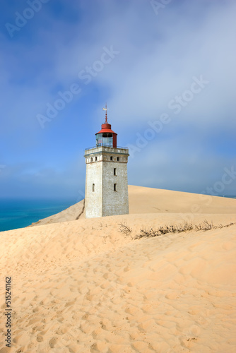 Deserted lighthouse by the sea with blue sky in the background on a sunny day. A lighthouse in between the sandy area surrounded by water and cloudy sky. The mysterious old tower alone in the desert © SteenoWac/peopleimages.com