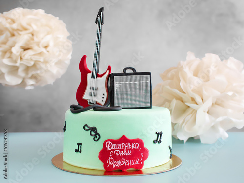 Musical themed cake with a guitar on top as a decoration. Sweet food for the musician's birthday. A gift to a creative person, a singer. Surprise for the guitarist. Top view, copy space, close up.