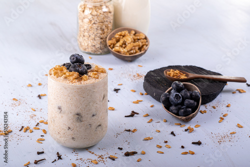 Overnight with blueberry fruits, cloves, and scattered cinnamon. In the background nuts, milk, and raw oats.