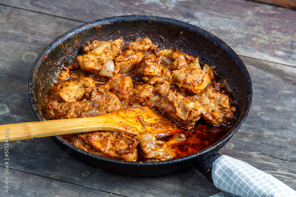 Fried chicken in a frying pan with a wooden spatula on a dark table.