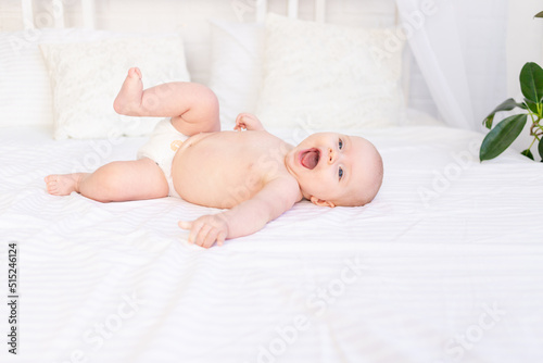 laughing baby girl in diapers in a crib on a white cotton bed lying on her back in the nursery smiling, newborn morning