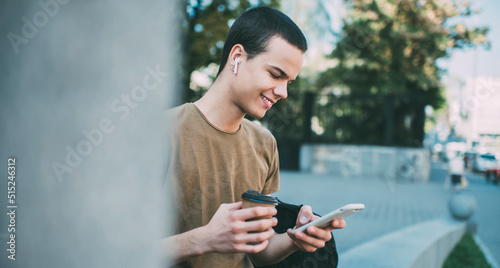 Cheerful man with takeaway coffee browsing smartphone on street