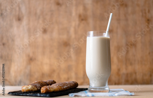 Side view. Glass with horchata, accompanied by two fartons, on a wooden background.  photo