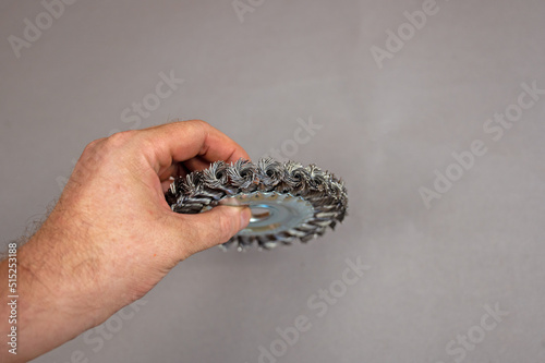 A man's hand holds the Disc Wire Brush. A tool for woodworking as well as stripping surfaces of corrosion, scale, or rust. Side view. Gray background. Selective focus.