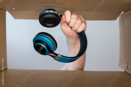 A man's hand pulls headphones out of a cardboard moving box. Wireless stereophonic device for personal listening to audio information. Bottom view. Inside view.  Close-up. Selective focus.