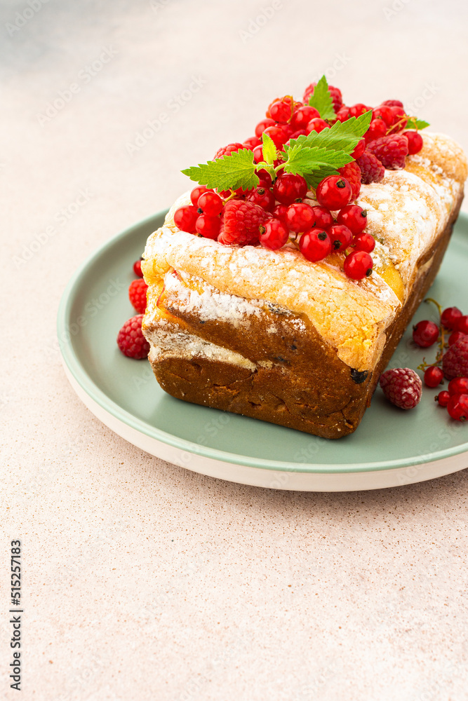 Rich sweet pie with fresh fruits, decorated with red currants and raspberries, in a plate on a pink background