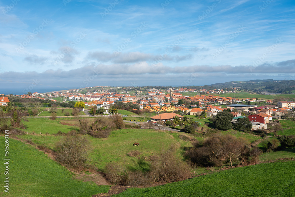 Beautiful top view of the picturesque town of Ajo surrounded by green fields under a blue sky crowded by clouds, Cantabria, Spain