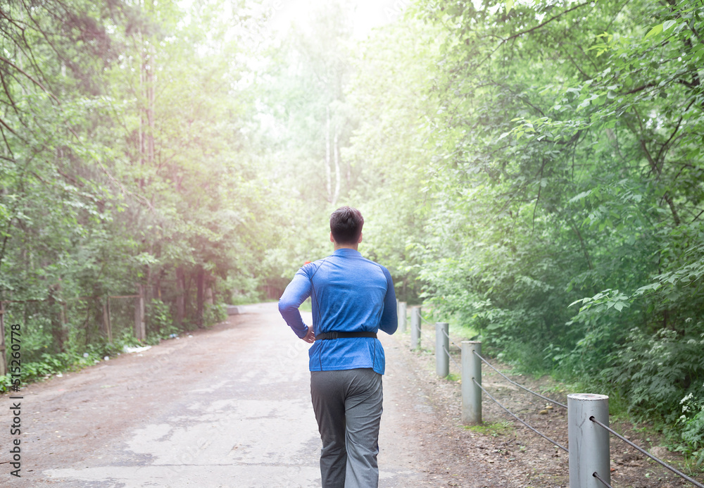 Back view of handsome man in blue sportswear jogging in the wood at the morning time Back view of handsome man in blue sportswear jogging in the wood at the morning time