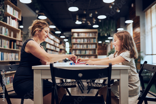 Teacher playing with schoolgirl board game in afterschool club. Child spending time playing game in school library after classes at primary school. Elementary education. Back to school