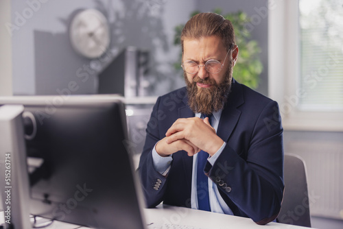 Caucasian businessman in formal wear with wry grimace sitting at workplace and looking on pc monitor. Facial expression, technology and people concert. photo