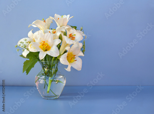 Fototapeta Naklejka Na Ścianę i Meble -  Bouquet white flowers lilies in glass vase on a blue table with space for text