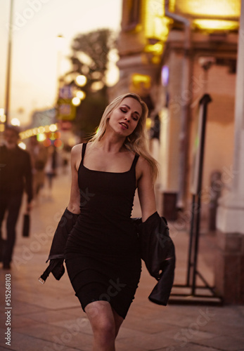 Smiling blond woman posing in fashion style clothes walking on city street summer night lights background. outdoor portrait. Vogue vintage