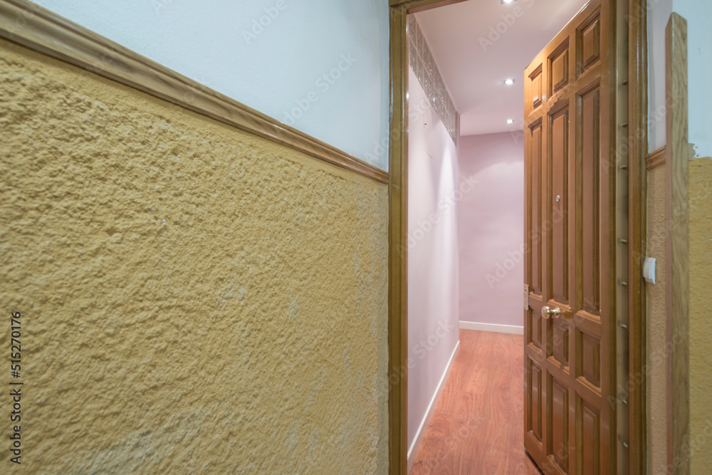 Obraz premium Entrance hall of a house with smooth pink painted walls, yellow rough exterior wall and vintage paneled wooden door