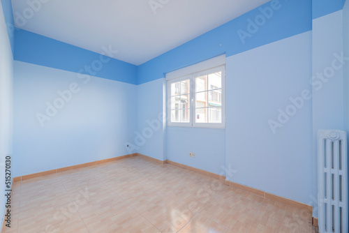 Empty room with light brown stoneware floors  cast iron radiator and walls painted in two shades of blue