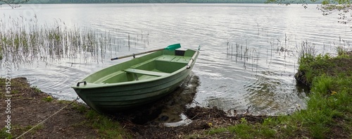 Small green boat anchored in forest lake. Scandinavia. Transportation, traditional craft, recreation, leisure activity, healthy lifestyle, local tourism, sport, rowing, hiking, summer vacations themes photo