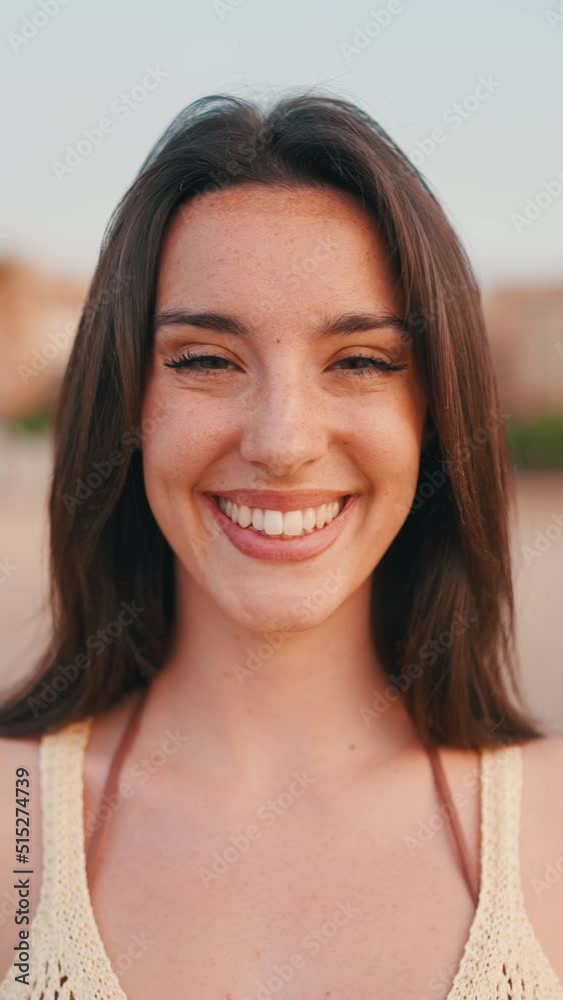 VERTICAL VIDEO: Close-up Beautiful brown-haired woman with long hair sits on the beach. Gorgeous girl with freckles and long eyelashes looks at the camera and smiles. slow motion VERTICAL VIDEO: Close-up Beautiful brown-haired woman with long hair sits on the beach. Gorgeous girl with freckles and long eyelashes looks at the camera and smiles. slow motion