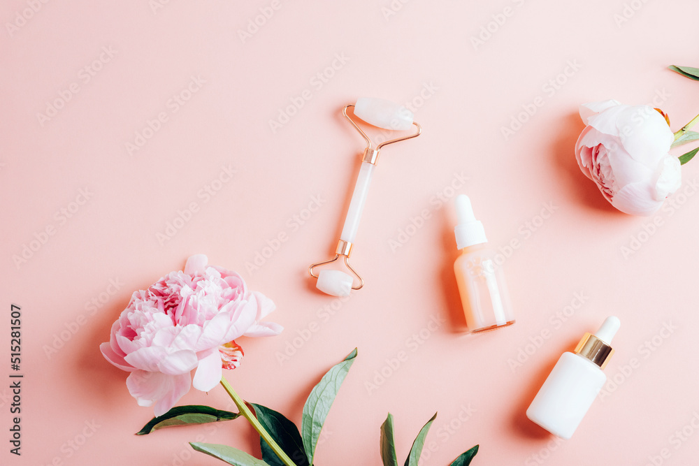 Dropper bottles with cosmetic oil, serum, facial roller and peony flowers on pink background. Top view, flat lay, copy space