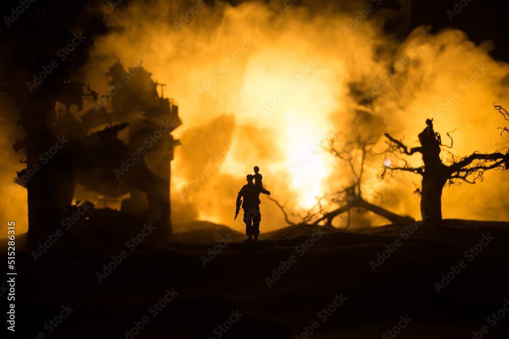 Obraz premium Silhouette soldier carrying little boy on his shoulder from fire. Rescue savior concept. Man moving out with little boy from burned out city destroyed in war. Selective focus