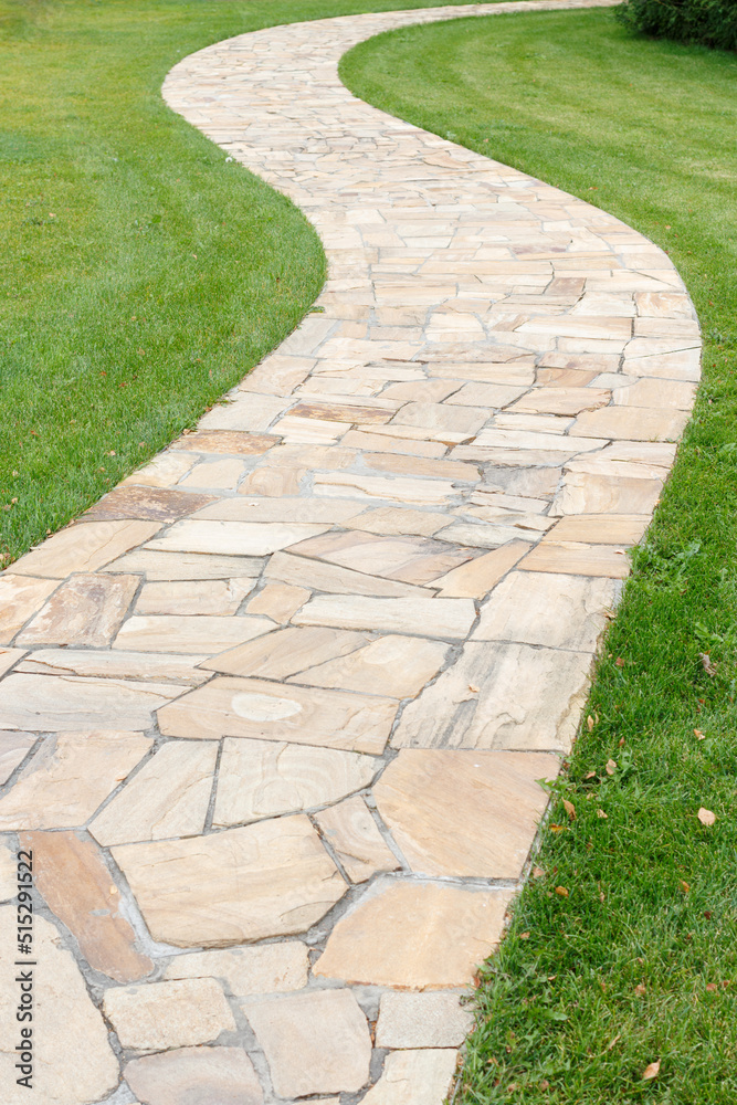 Winding stone path in the middle of a flat green lawn. Selective focus. Winding stone path in the middle of a flat green lawn. Selective focus.