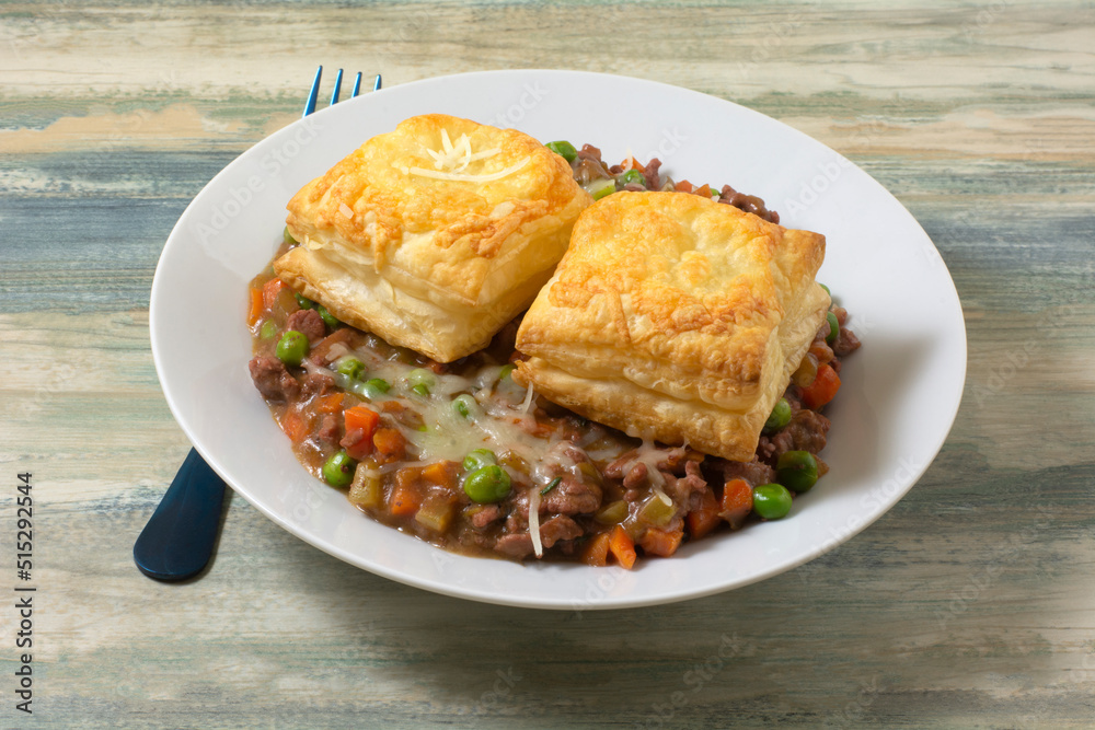 Beef and vegetable stew with puff pastry in white bowl with blue fork Beef and vegetable stew with puff pastry in white bowl with blue fork