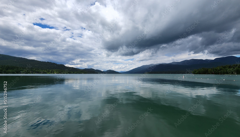 Obraz premium Whitefish Lake in Flathead County, Montana under dramatic summer cloudscape reflected in calm water of lake.