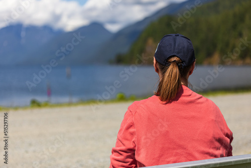 Rear portrait of young woman sitting relaxed on a park bench in sunny summer day. Girl enjoying beautiful view in a park © Elena_Alex