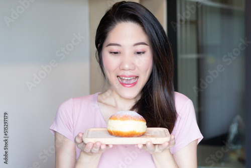 Asian beautiful woman are holding doughnut bun on wooden plate and smile with happy .
