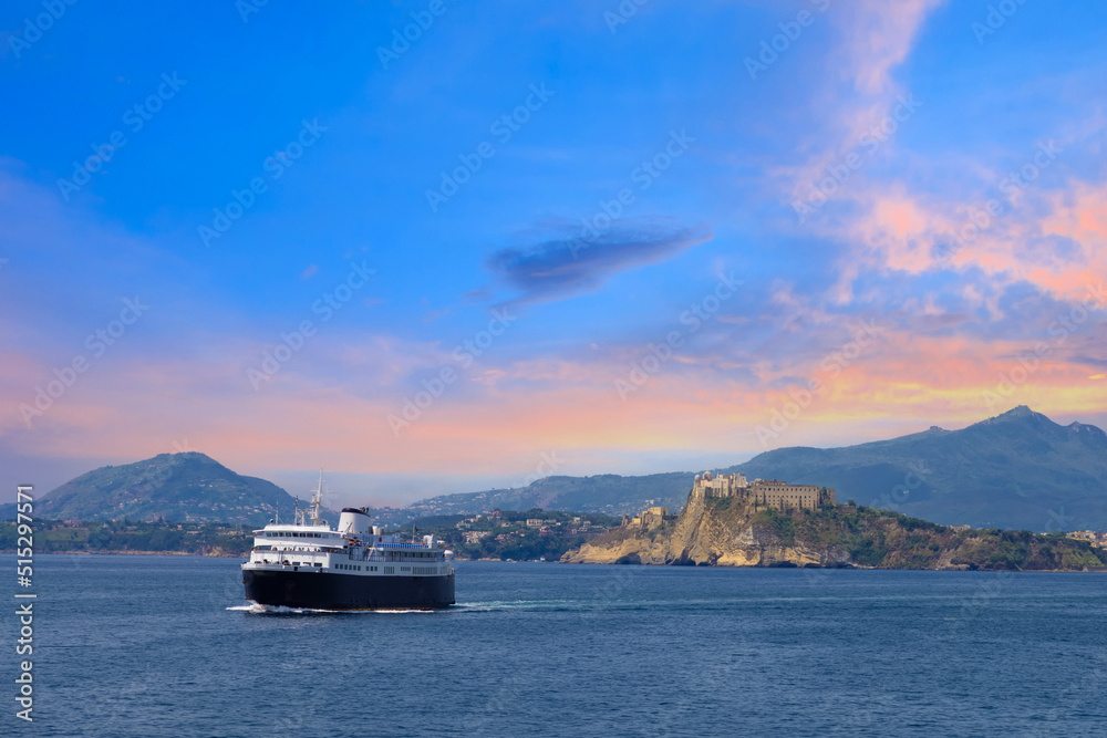 Italy, scenic sunset over Procida Island near Naples with boat approaching it from afar.