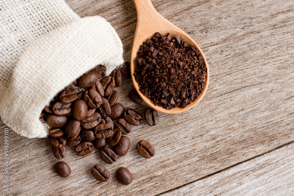 Fototapeta premium Roasted coffee bean in hemp sack and granuleatd coffe in scoop on wood table background. Top view. Flat lay.