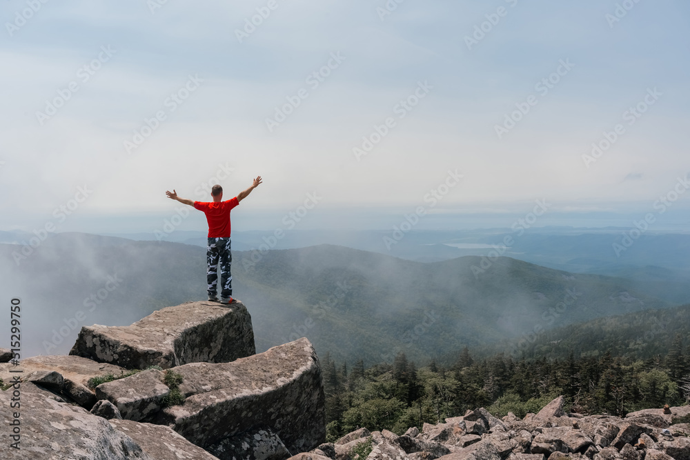 Fototapeta premium Hiker man on the top of the mountain enjoys the aerial view, raising his hands above the clouds. Mount Pidan