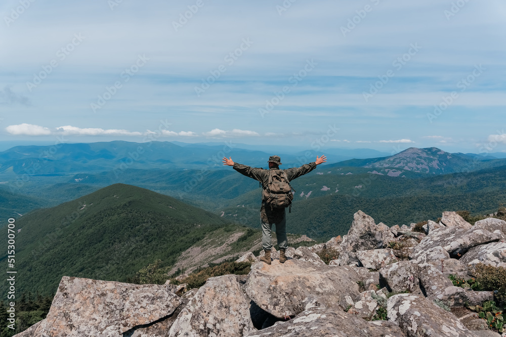 Obraz premium A man stands on top of a mountain and enjoys a beautiful mountain view. Taken on top of Mount Pidan, Russia.