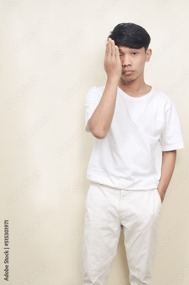 portrait of man wearing white t-shirt covering one eye with hand portrait of man wearing white t-shirt covering one eye with hand