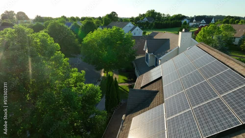 Rooftop solar panels on home in American neighborhood. Sun reflects light. Green renewable energy theme. Aerial.