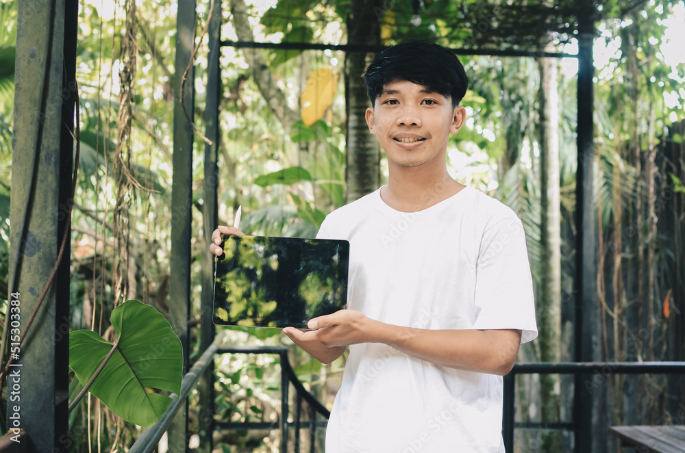 smiling asian man showing tablet screen on nature background smiling asian man showing tablet screen on nature background