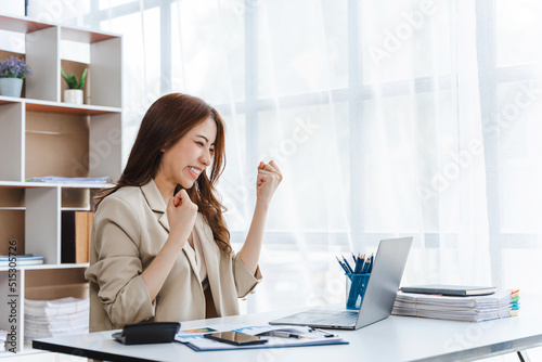 Portrait of success Asian businesswoman enjoy success with laptop on work desk. Authentic shot joyful woman got jackpot, Surprised and celebrating her victory. © makibestphoto