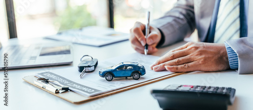 Man signing car insurance document or lease paper. Writing signature on contract or agreement. Buying or selling new or used vehicle. Car keys on table. Warranty or guarantee. Customer or salesman. photo