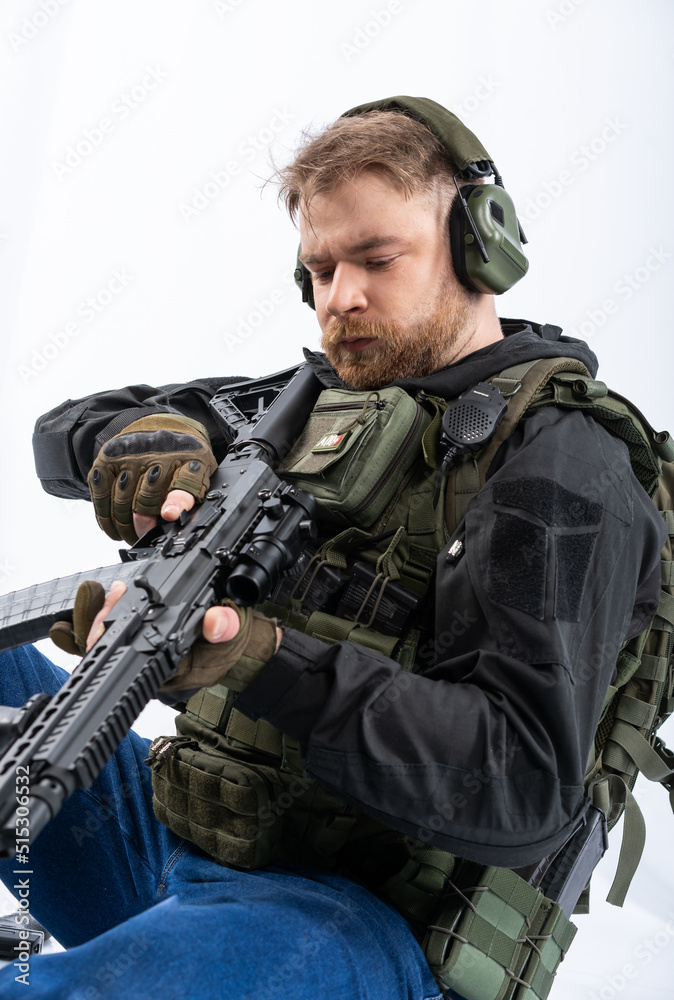 airsoft player in full gear with GG RK74 fire series guns. a man in headphones, a bulletproof vest, with a backpack and a belt, aims his machine gun to the side. profile. White background.