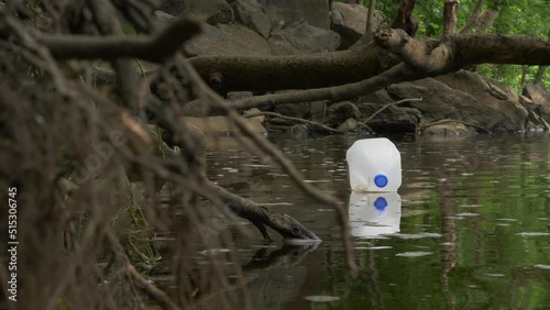 Milk jug slowly floats down river past tree roots slow motion photo