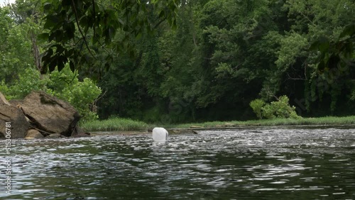 milk jug floats down river slowly towards old concrete bridge on a cloudy day wide photo