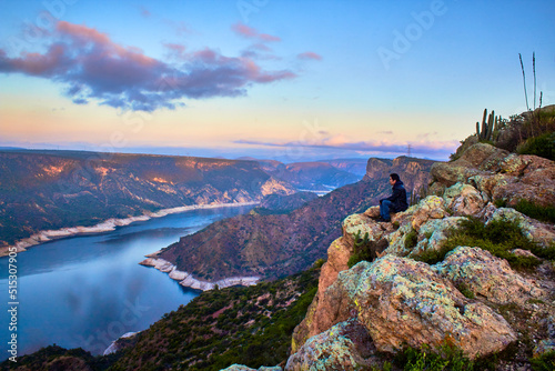 young man sitting in top of a mountain watching a landscape with river and mountains at the morning in zimapan hidalgo  photo