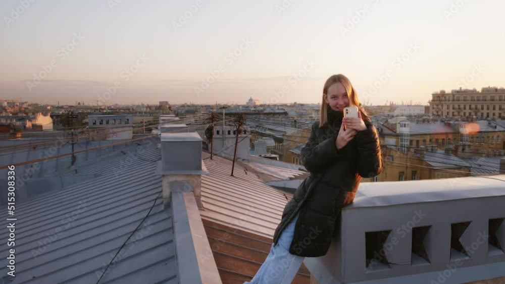 Happy Teen Girl Taking Pictures On Her Smartphone On The Roof In Europe City. She Is Laughing Admiring Amazing View Of Ancient Town With Historic Buildings. Tourism Traveling And Wanderlust Concept. Happy Teen Girl Taking Pictures On Her Smartphone On The Roof In Europe City. She Is Laughing Admiring Amazing View Of Ancient Town With Historic Buildings. Tourism Traveling And Wanderlust Concept.
