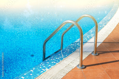Stainless ladder and handrails in outdoors swimming pool on  summer sunny day. Seaside vacation and hotel resort concept. Entrance in blue clean sea water pool © Elena