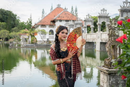 Portrait young asia girl with balinese traditional clothes standing in front of the garden bridge photo