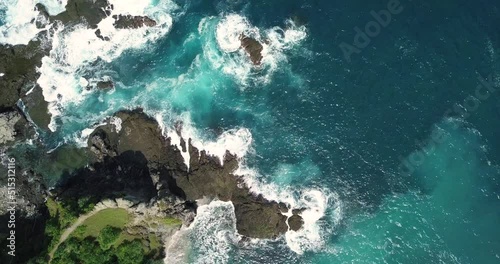 Aerial overhead shot of waves of Indian Ocean hitting boulder and rocks in the beach in sunny condition weather - Pengilon Hill, Indonesia, Asia photo