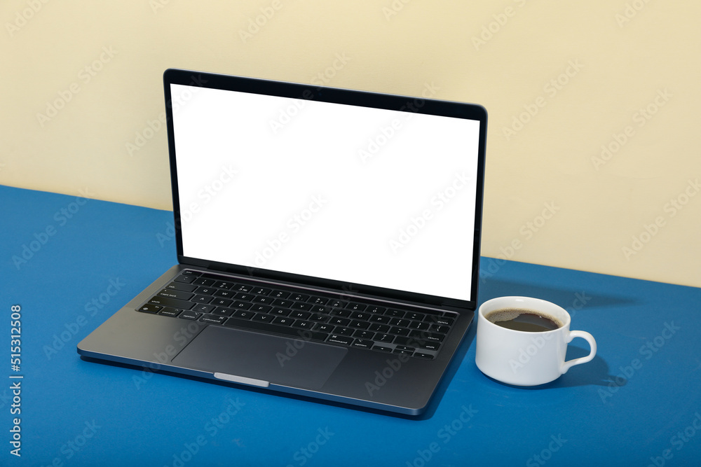 Laptop with blank screen and cup of coffee on two tone background Laptop with blank screen and cup of coffee on two tone background