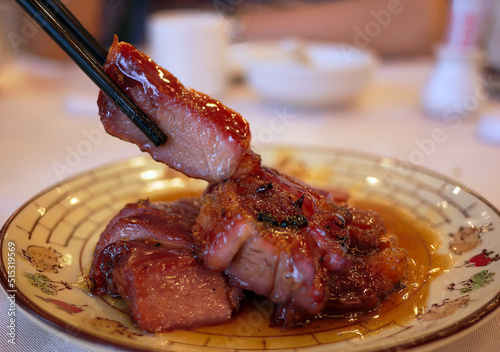 close-up side view chopsticks holding piece of juicy delicious barbecue roasted pork cantonese style photo