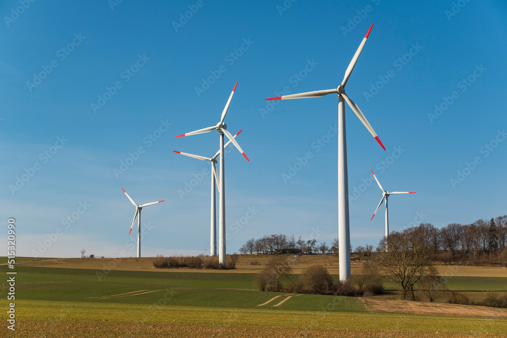 Group of wind turbines against a bright blue sky in a rural landscape, suitable as a symbolic image for renewable energies and topics related to climate change, near Höxter, Weserbergland, Germany Group of wind turbines against a bright blue sky in a rural landscape, suitable as a symbolic image for renewable energies and topics related to climate change, near Höxter, Weserbergland, Germany